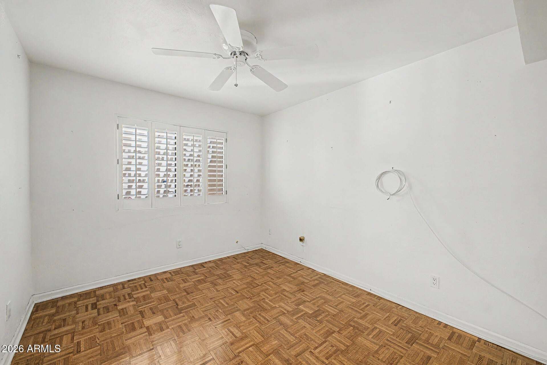 20 of 30. Bright guest bedroom showcasing plantation shutters, warm parquet flooring, and a neutral palette. A comfortable space ready to serve as a bedroom, office, or creative workspace.