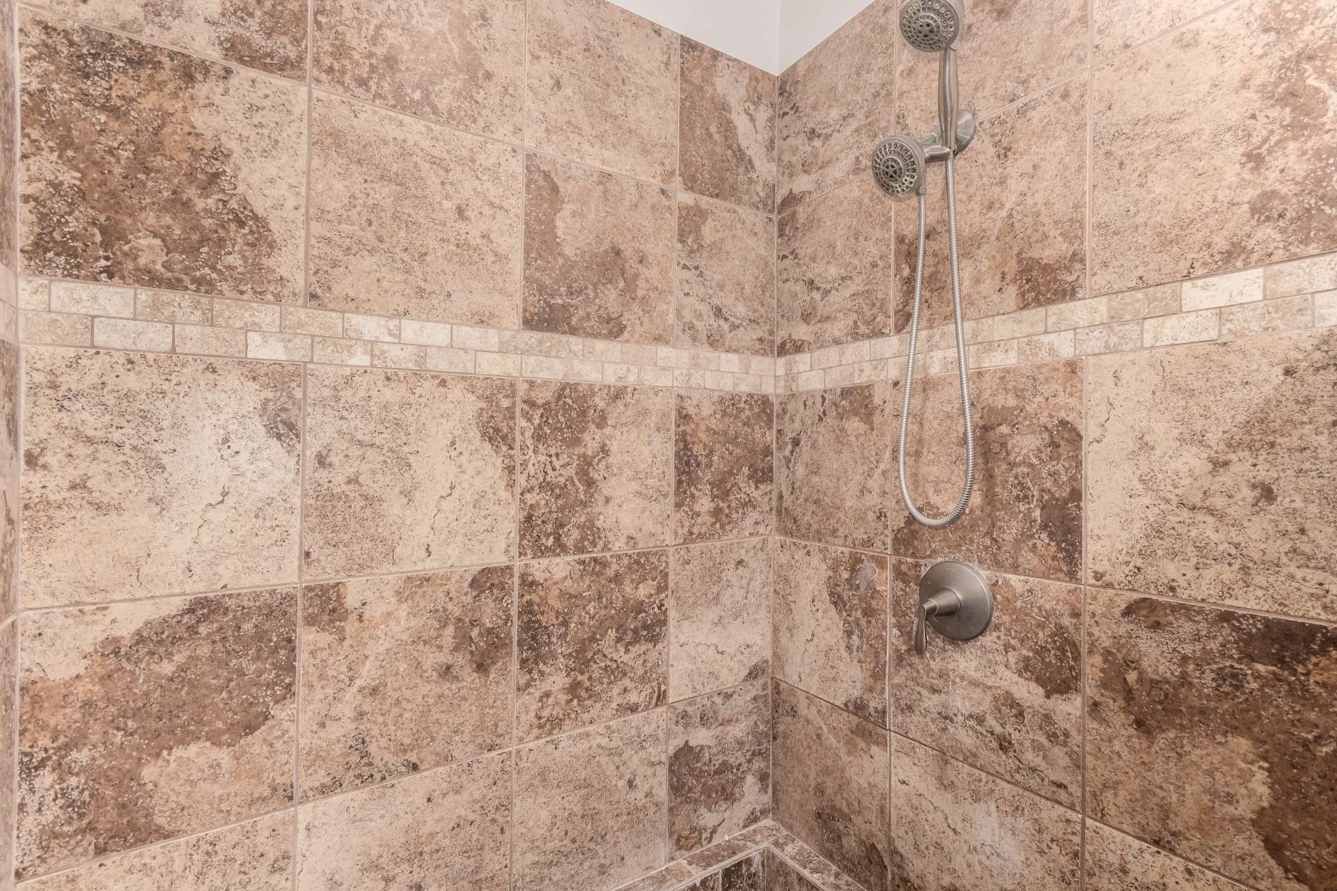 22 of 34. Floor-to-ceiling tiled walk-in shower with upgraded fixtures and decorative tile accents creates a luxurious spa-like atmosphere within the remodeled primary bathroom.