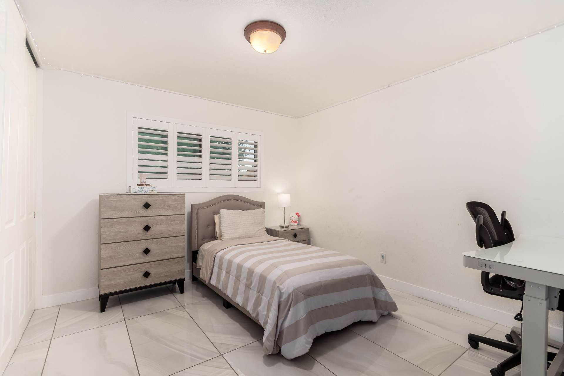 23 of 34. Bright secondary bedroom featuring plantation shutters, updated tile flooring, and versatile space ideal for guests, children, or a dedicated home office.
