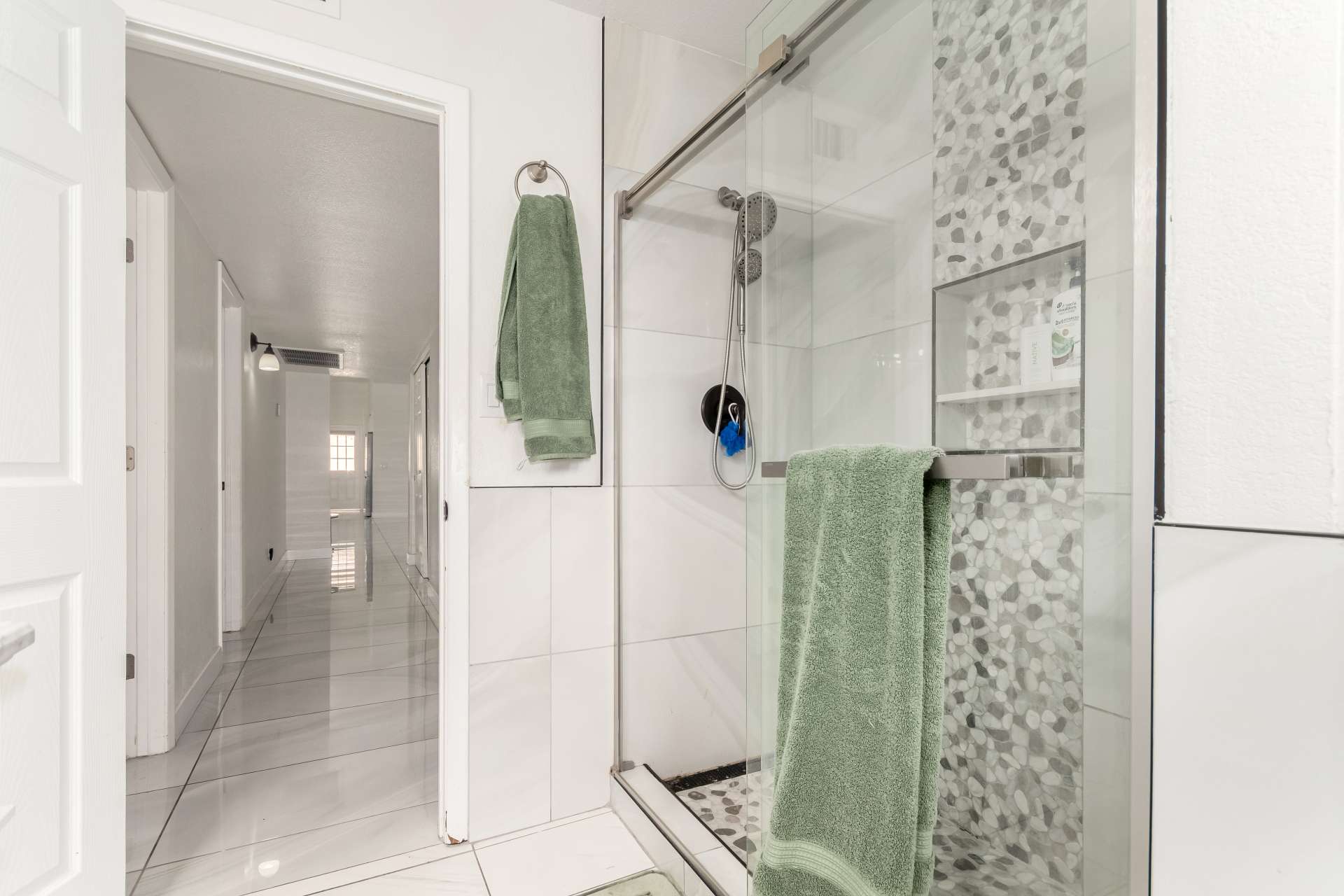 27 of 34. Designer walk-in shower with frameless glass enclosure, decorative pebble tile accents, built-in storage niche, and modern fixtures that enhance this updated Scottsdale home.