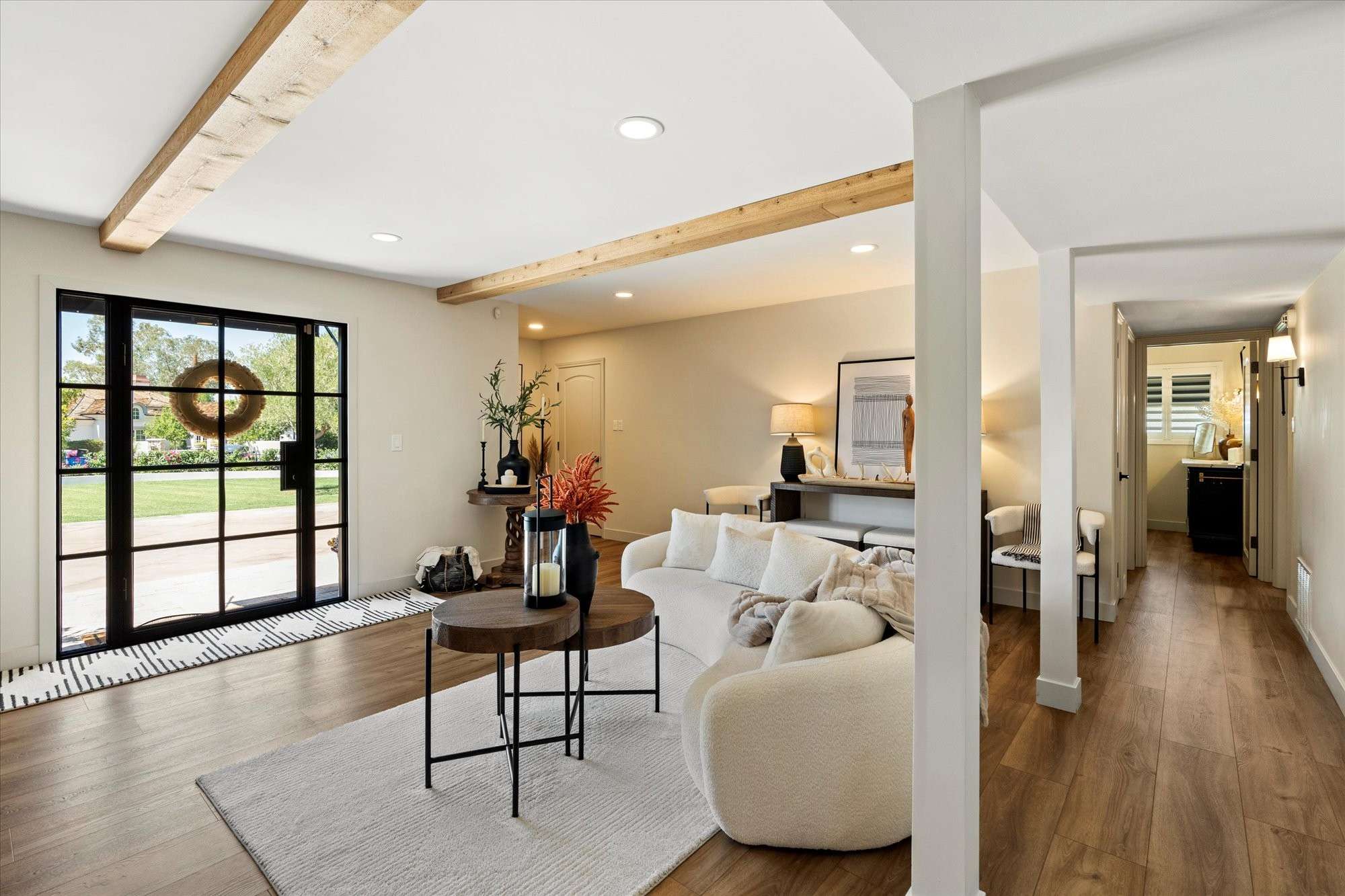 2 of 48. Warm and welcoming living room featuring exposed ceiling beams, wide plank floors, and oversized doors opening to lush outdoor views.