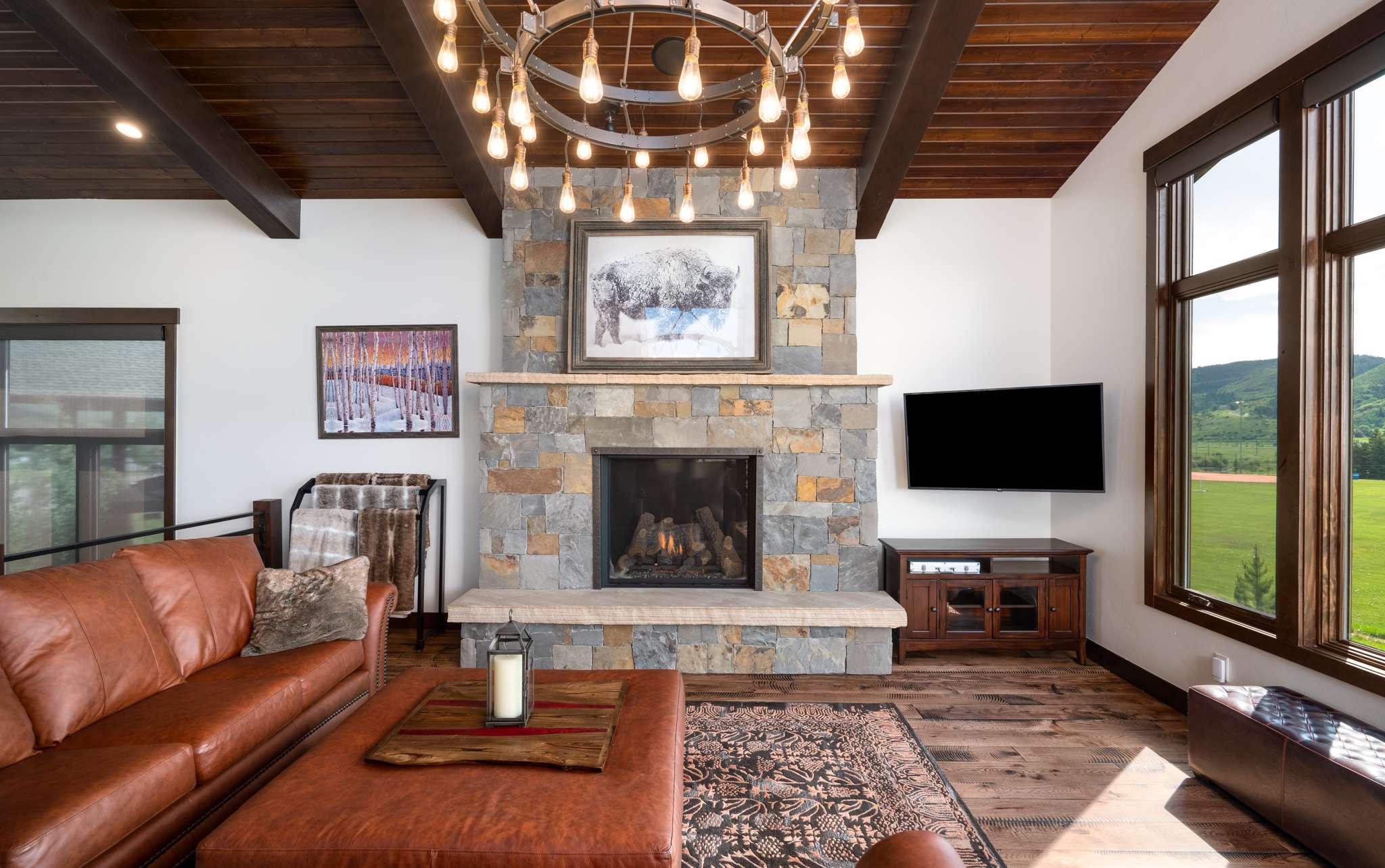 8 of 42. Spacious great room with mountain views, a stone fireplace, and modern fixtures, perfect for gatherings. The open floor plan connects the great room to the kitchen and dining areas. Sliding glass doors open to a back deck featuring Emerald Mountain views.