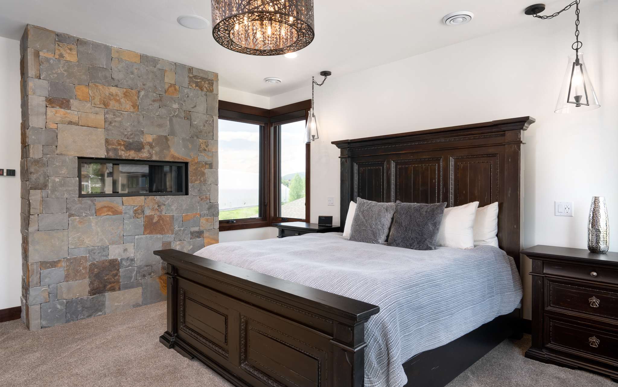 15 of 42. Luxurious primary bedroom featuring a stunning stone fireplace and modern lighting, a five-piece en suite bath, mountain views, and a private balcony.