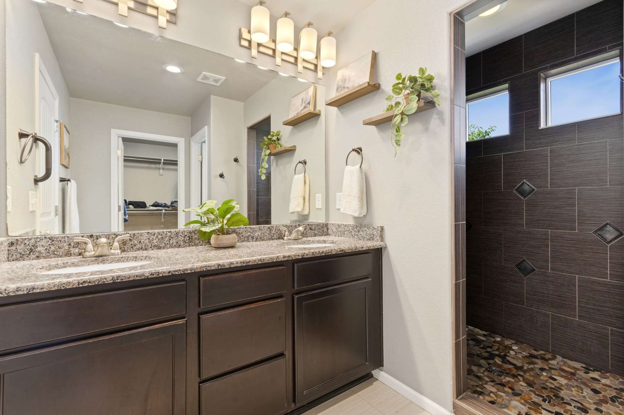 22 of 34. Primary bathroom features a dual vanity, a spa-like walk-in shower paved in river rocks, and an oversized closet that simplifies daily routines.