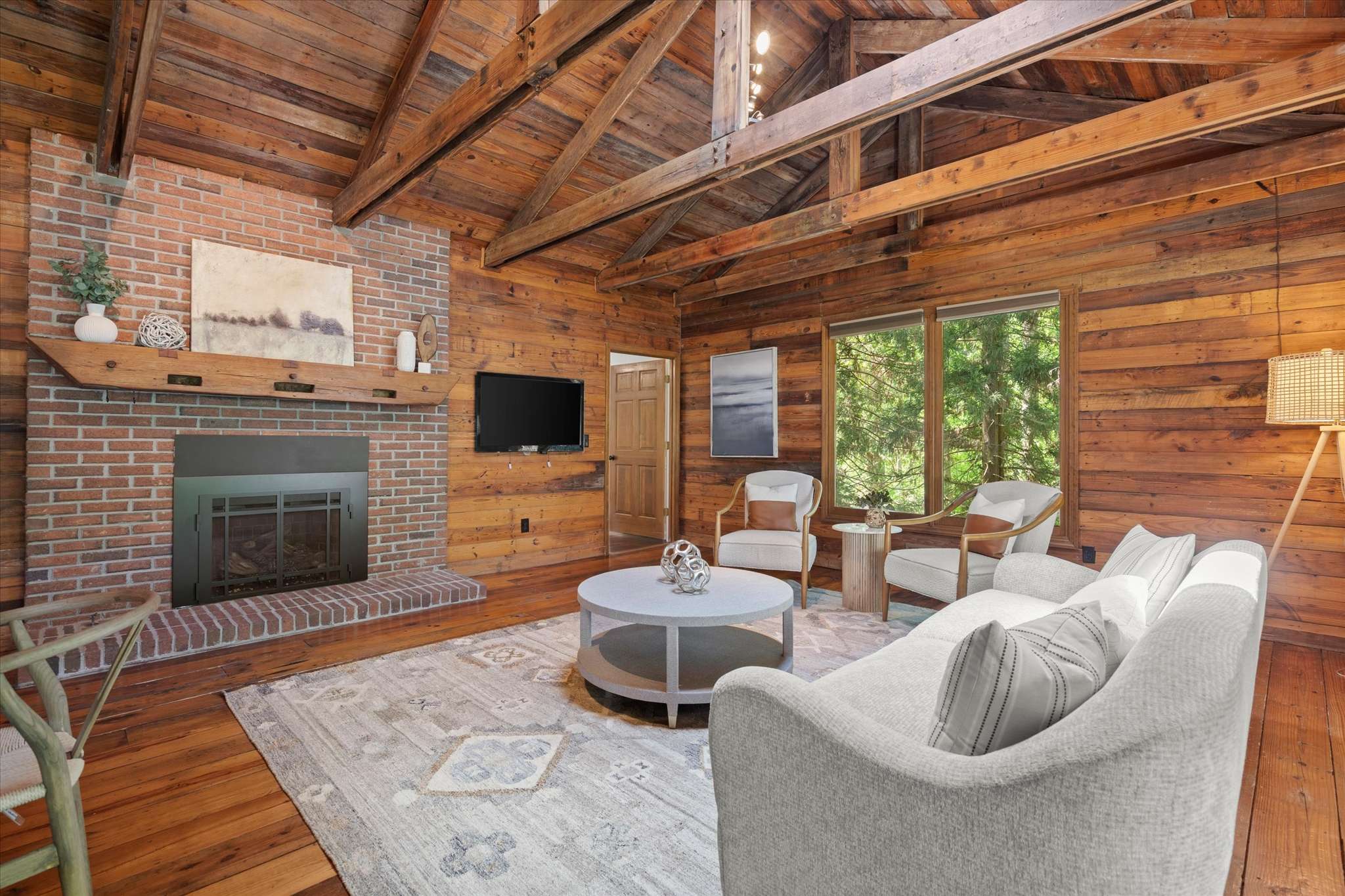 13 of 72. Cozy living space features exposed beams, a brick fireplace, and large windows for natural light.