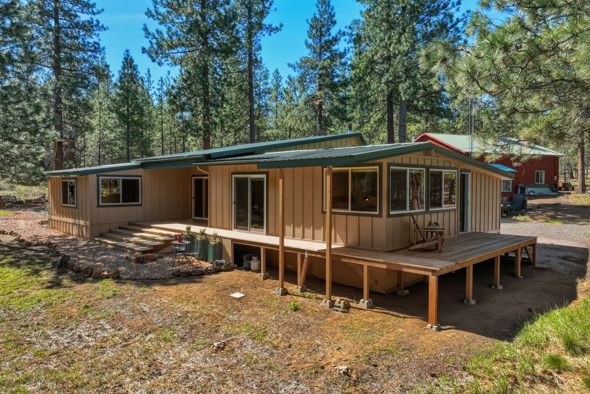 55 of 61. Spacious home nestled among tall pines, featuring ample outdoor space and a welcoming deck that wraps from the great room to the second bedroom, around to the primary suite.