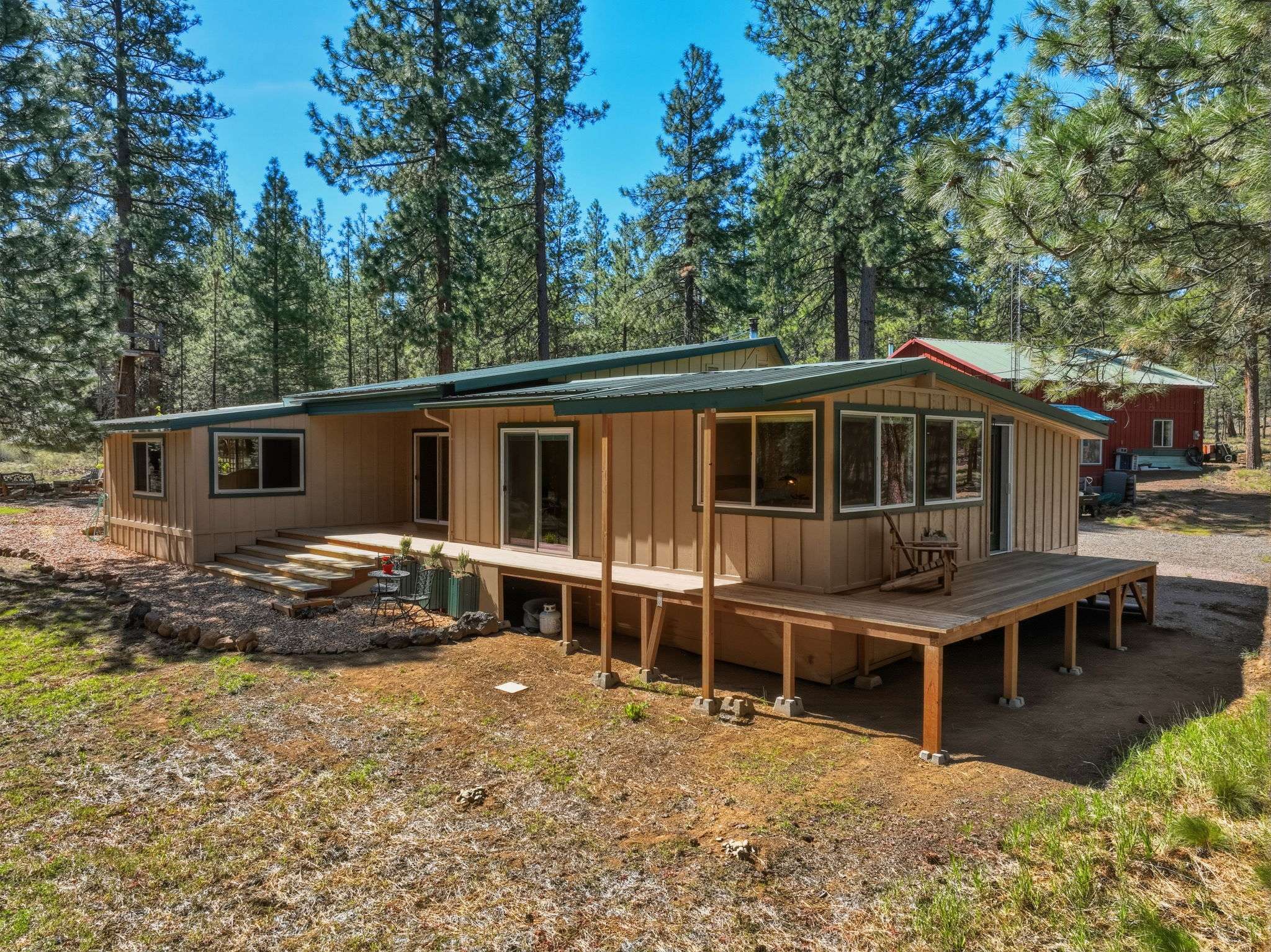 55 of 61. Spacious home nestled among tall pines, featuring ample outdoor space and a welcoming deck that wraps from the great room to the second bedroom, around to the primary suite.