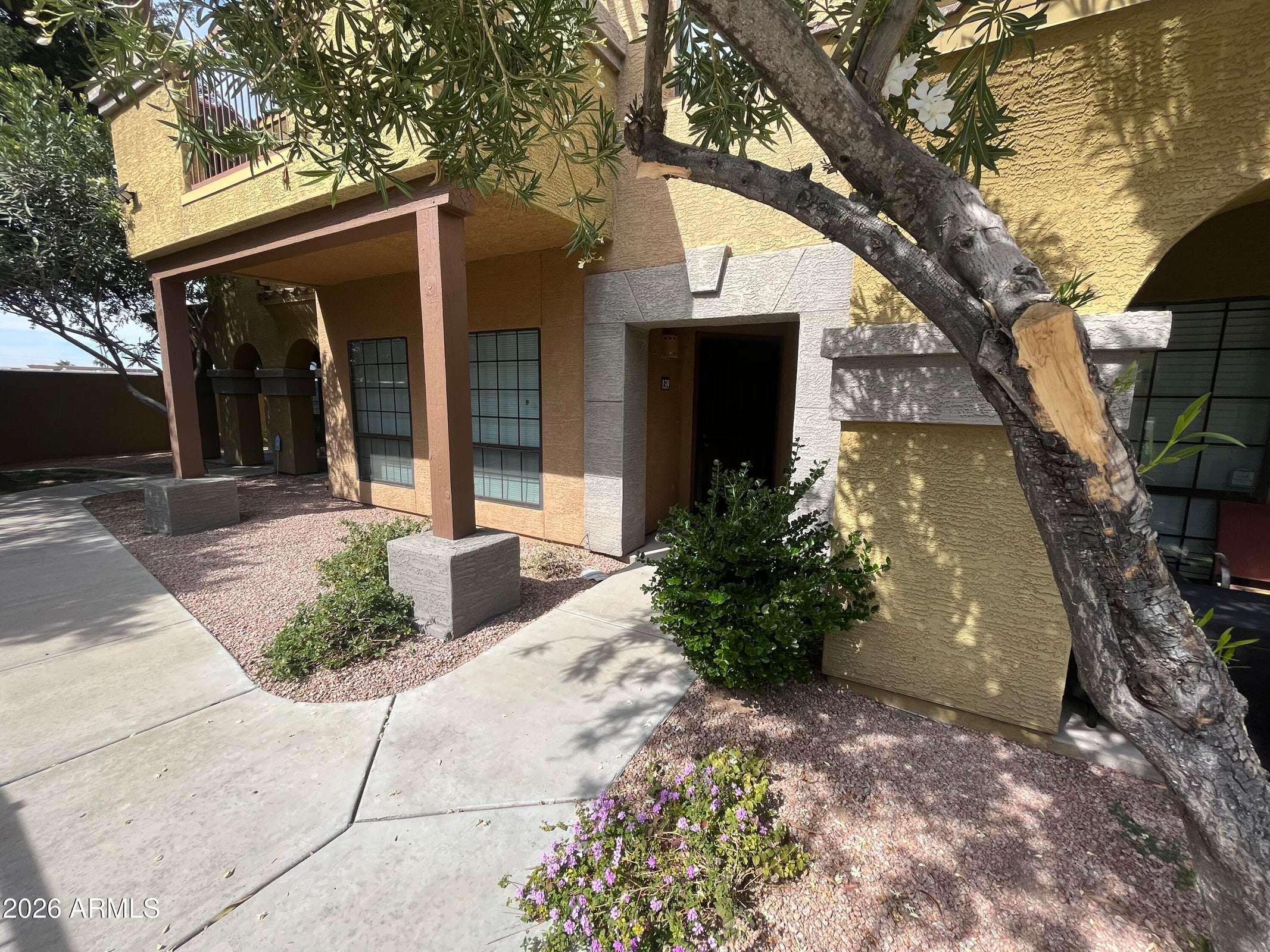 2 of 26. The private front entrance is framed by mature landscaping and desert-friendly grounds, creating a welcoming first impression in this well-maintained gated community.