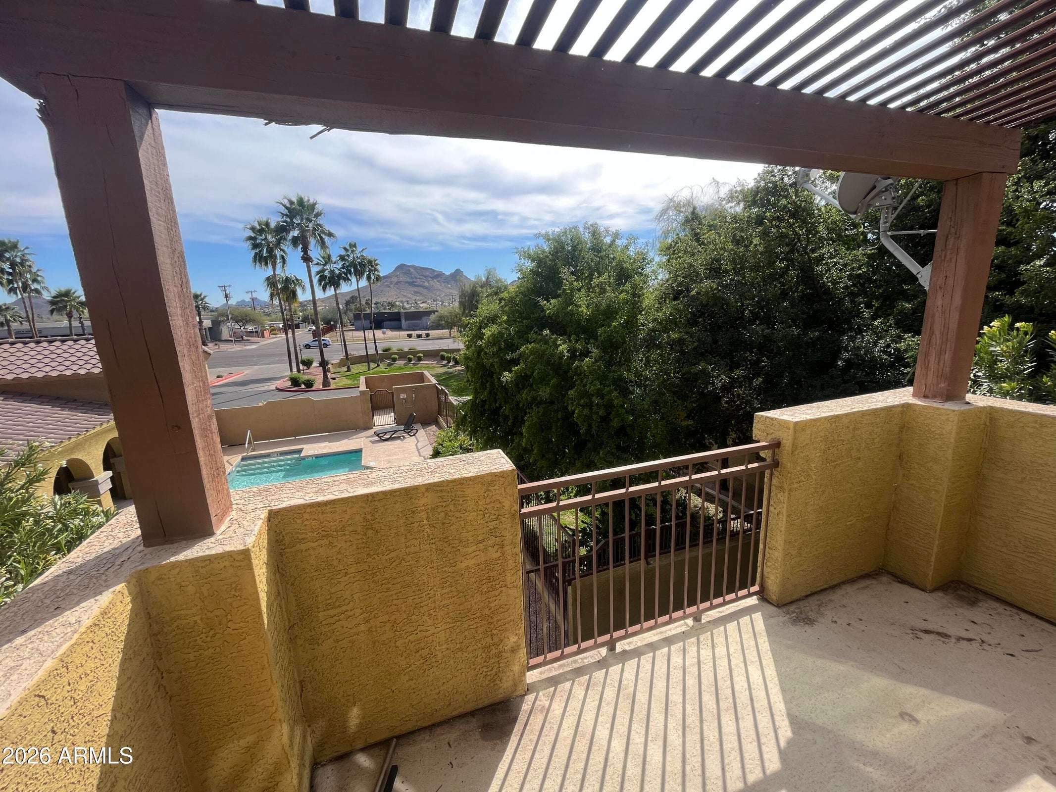 7 of 26. The spacious upper balcony with pergola offers relaxing views of the community pool, mature landscaping, and nearby mountain scenery, perfect for enjoying Arizona mornings and evenings.