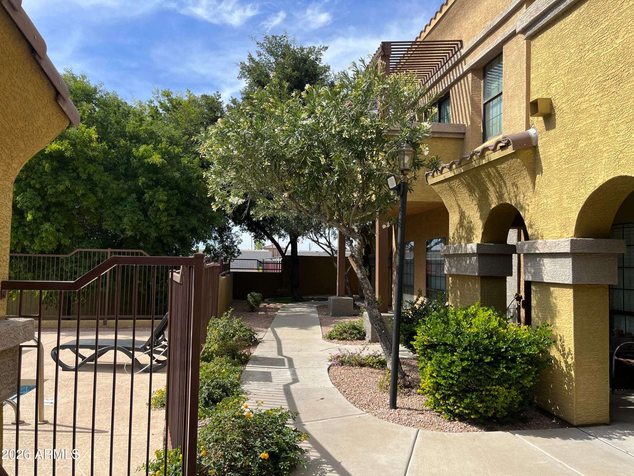 13 of 26. Well-maintained pathways wind through mature landscaping, connecting residents to the pool and shared amenities while creating a welcoming neighborhood atmosphere within the gated community.