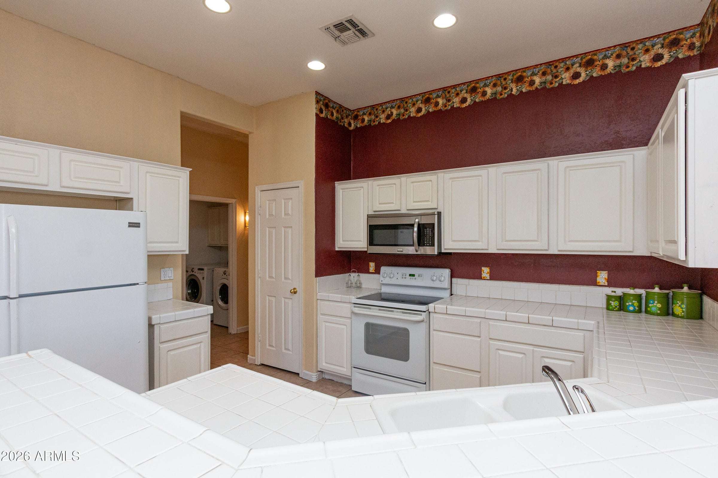 11 of 29. Open kitchen showcasing extensive tile counters, breakfast bar seating, abundant cabinetry, and recessed lighting. Designed to keep the chef connected to family and guests throughout the home.