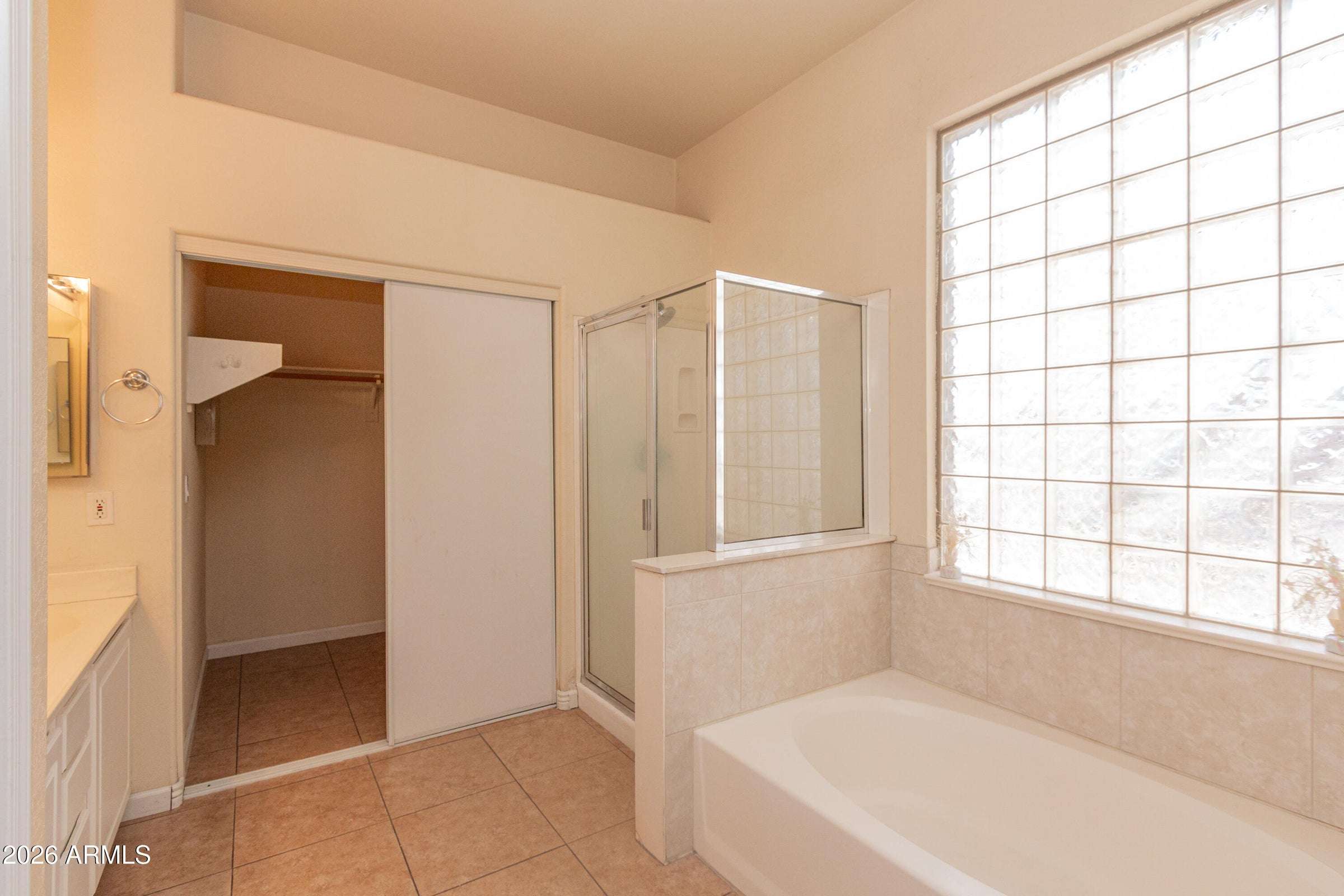 17 of 29. Primary bath featuring a relaxing soaking tub, separate glass-enclosed shower, and natural light from a glass block window. A comfortable space for unwinding after a long day.