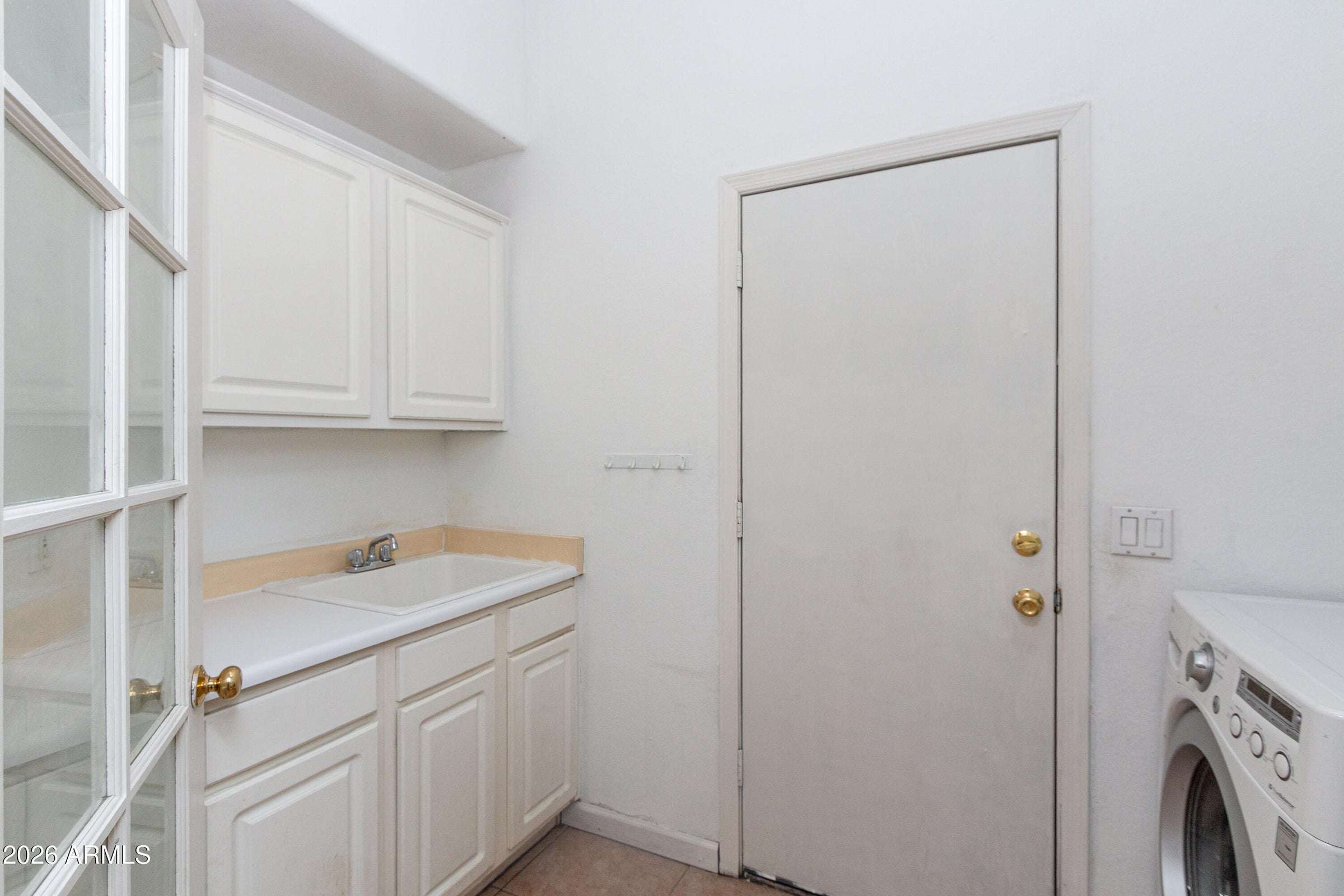 24 of 29. Dedicated laundry area with cabinetry, utility sink, and workspace for household tasks. Direct outdoor access adds practicality and convenience to this thoughtfully designed home.