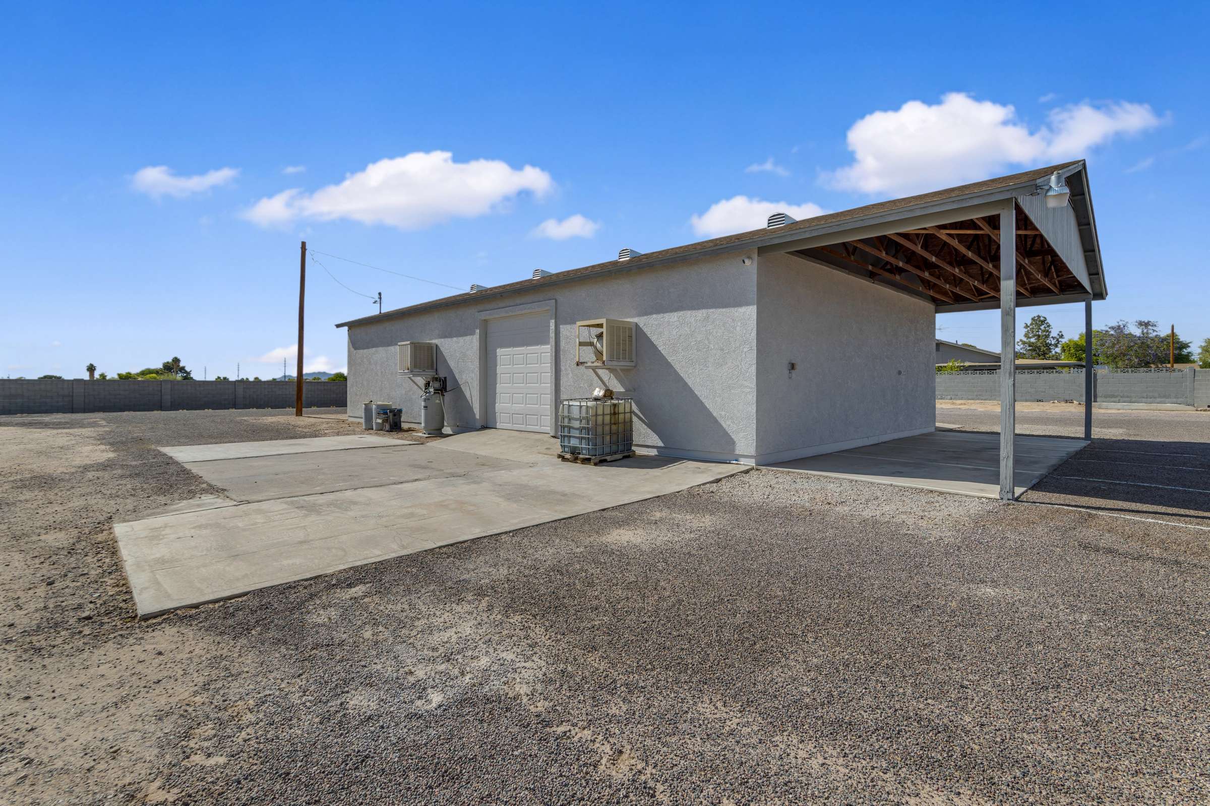 9 of 43. Rear exterior showcases additional workshop access, generous concrete work areas, covered storage, and room for trailers, RVs, equipment, or future outdoor improvements on this versatile property.