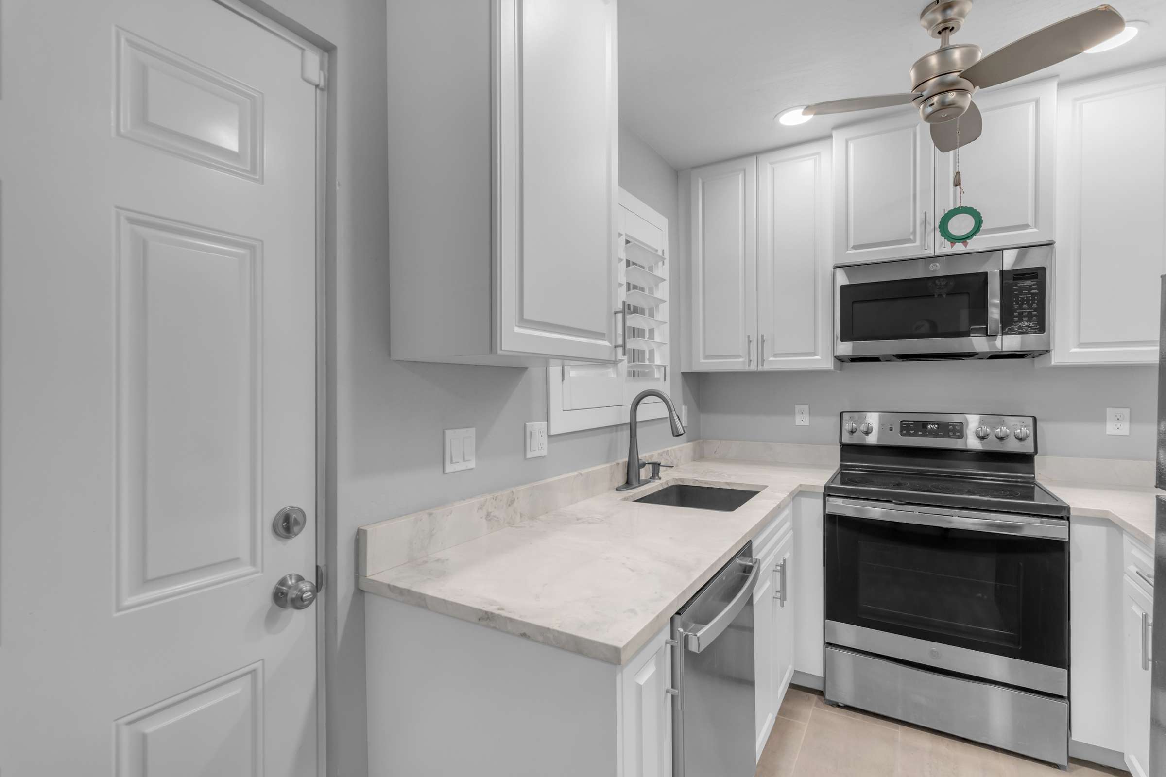 14 of 43. Updated kitchenette features sleek white cabinetry, stainless steel appliances, modern countertops, and efficient storage, creating a stylish and functional living environment.