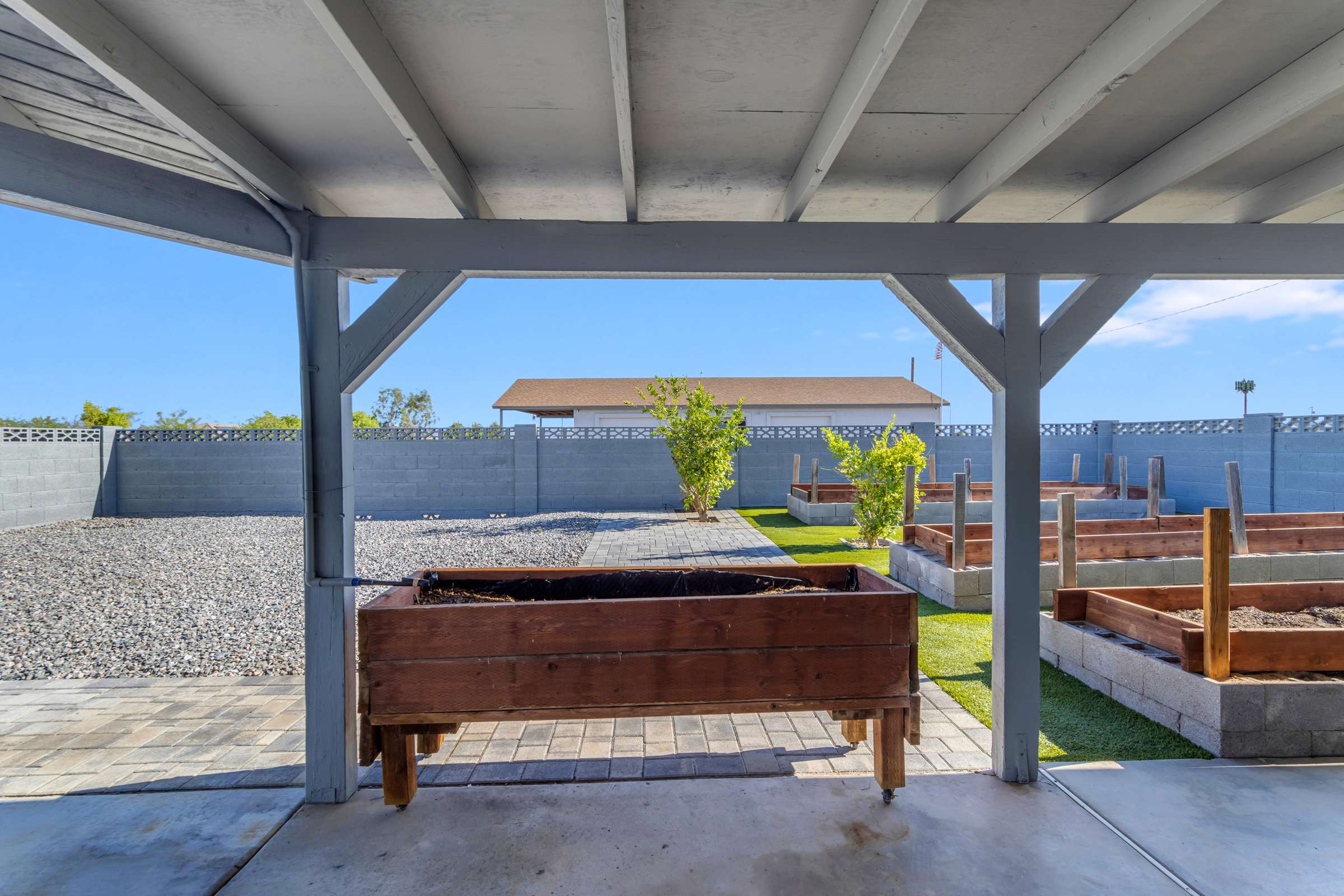 29 of 43. Covered patio overlooks raised planter boxes, paver pathways, and spacious backyard landscaping, offering an inviting outdoor area perfect for gardening, entertaining, and enjoying Arizona living in Goodyear.