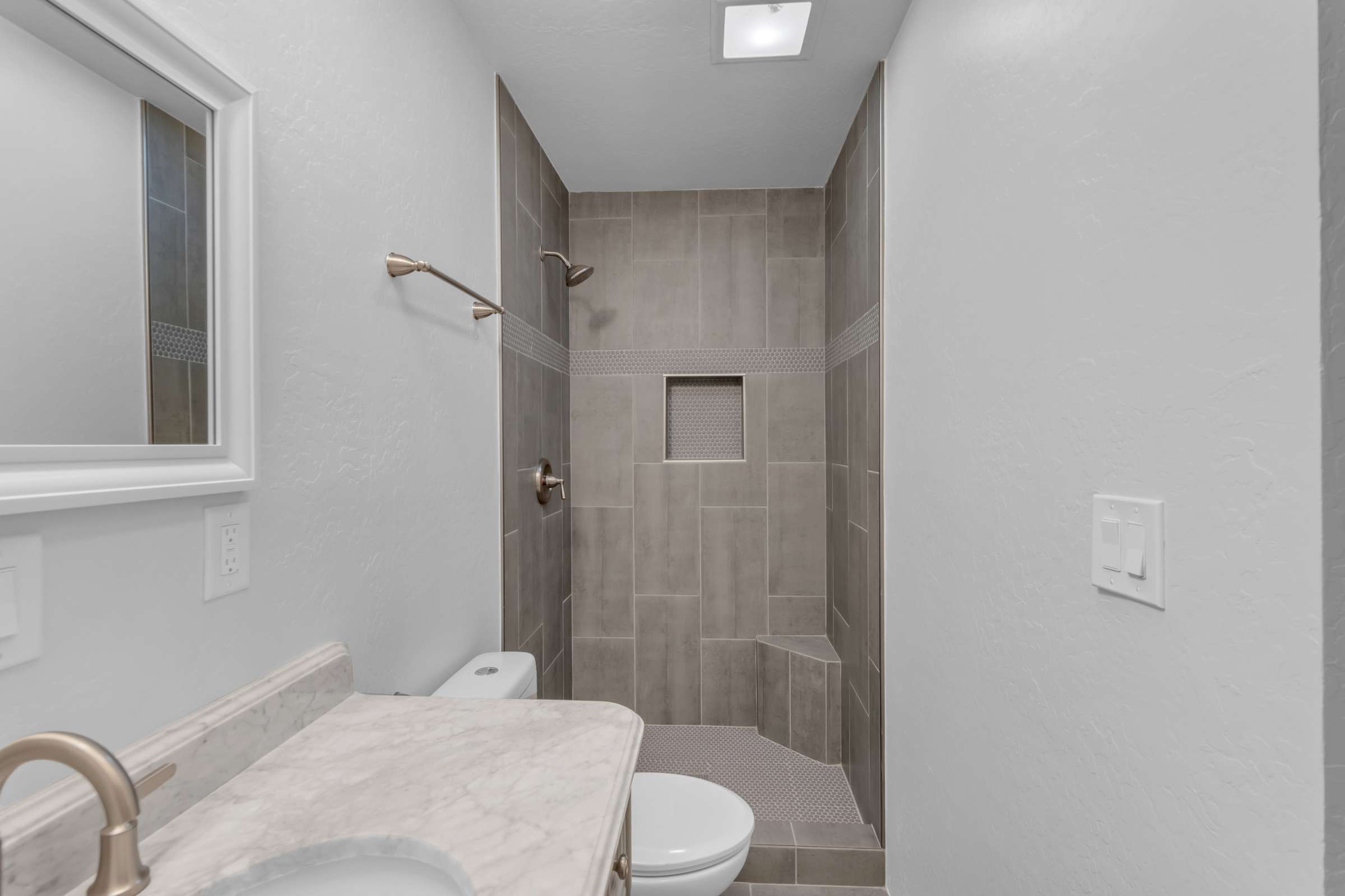 32 of 43. Stylish walk-in shower showcases floor-to-ceiling tile, built-in storage niche, and modern finishes, creating a comfortable and elegant bathroom designed for everyday living.