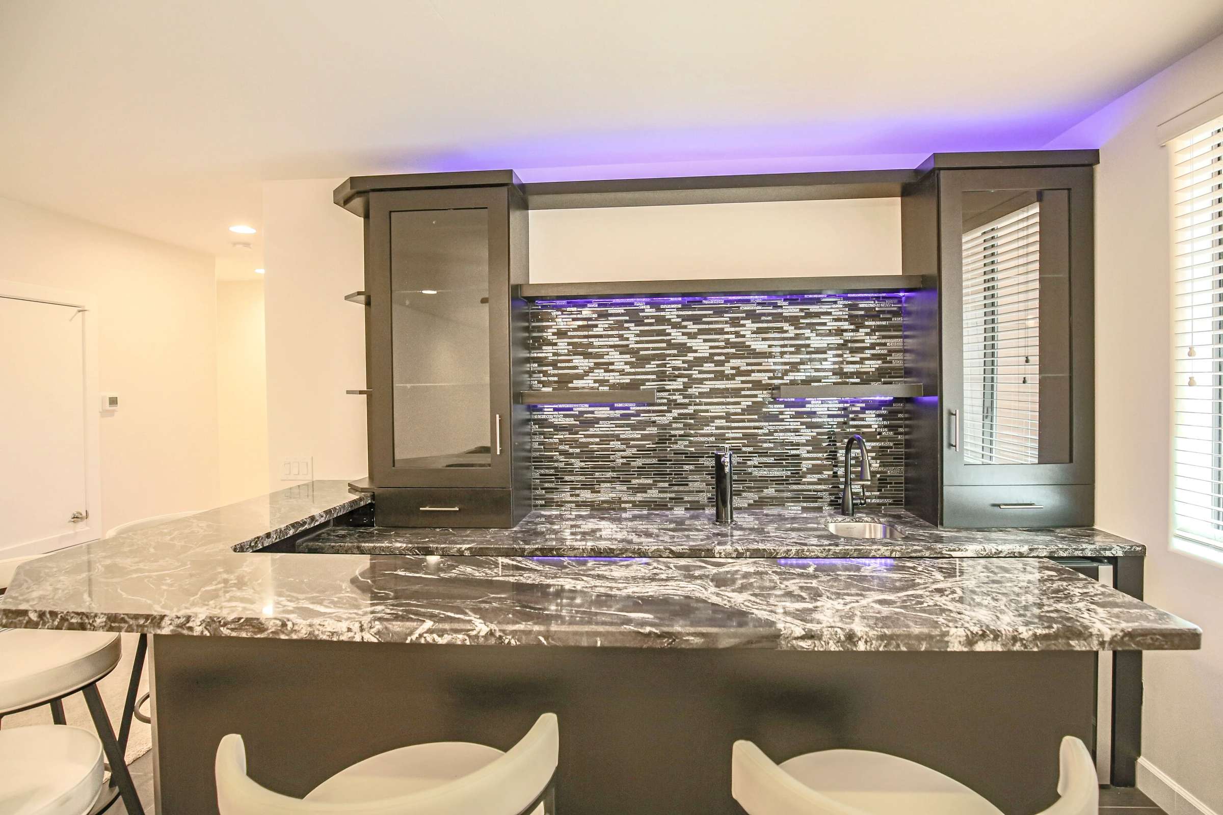 44 of 72. A stunning custom wet bar features granite countertops, beverage sink, glass cabinetry, designer backsplash, accent lighting, and bar seating perfect for entertaining guests.