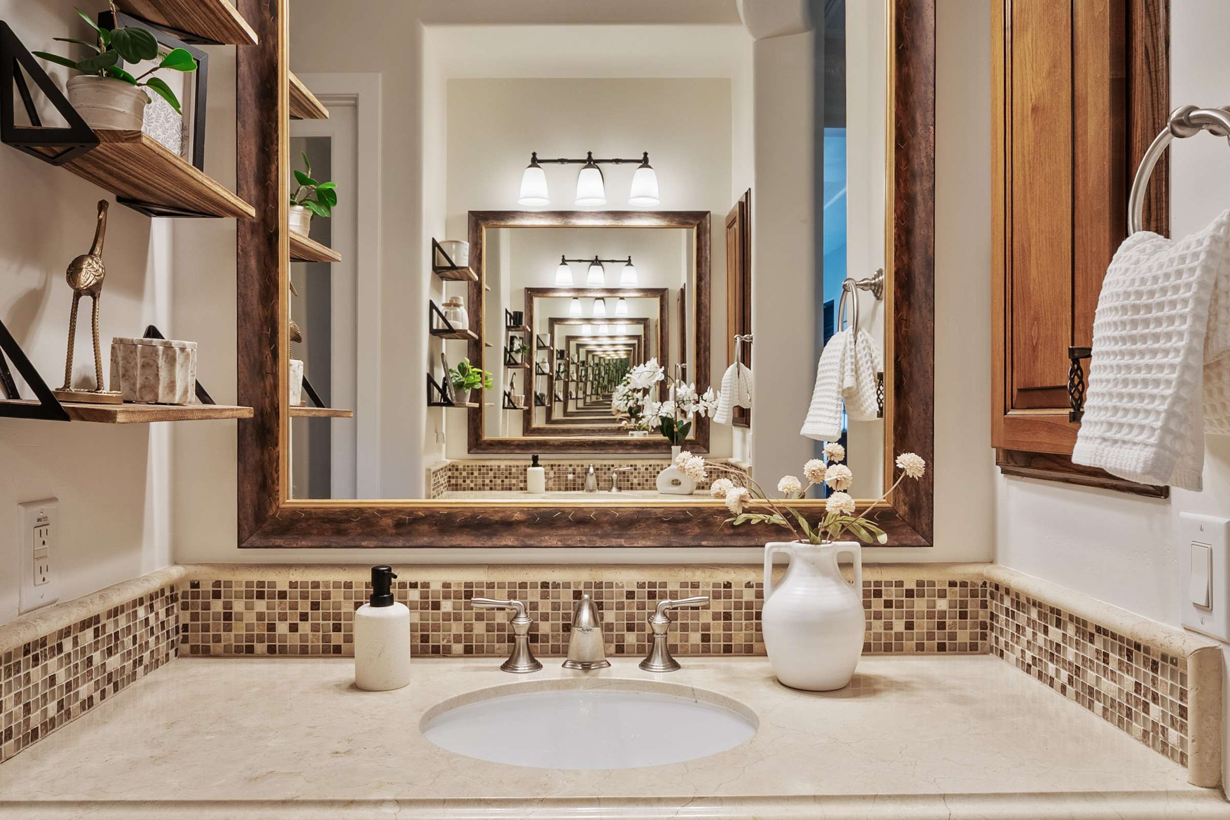 32 of 72. Designer lighting, custom cabinetry, stone countertops, decorative shelving, and an oversized framed mirror combine to create a sophisticated vanity space in the primary bathroom.