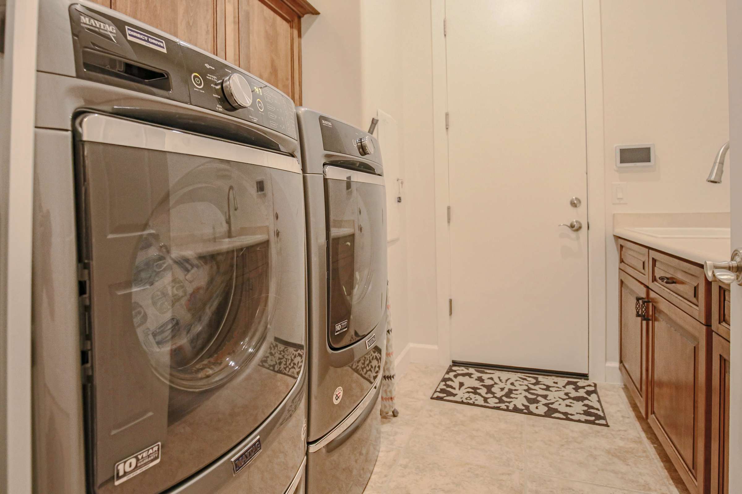 42 of 72. Designed for convenience, this laundry room includes front-loading appliances, built-in cabinetry, utility sink, tile flooring, and extra workspace for everyday household tasks.