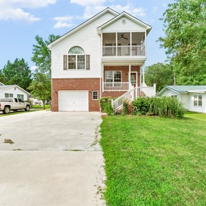 Multi-story home with a spacious yard, featuring an inviting front porch and attached garage.