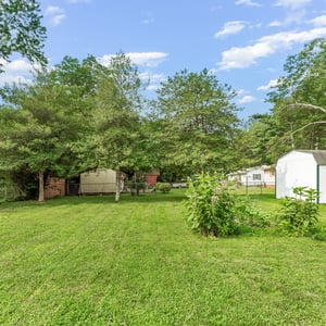 Spacious outdoor area featuring mature trees, a large lawn, and storage shed, ideal for various uses.