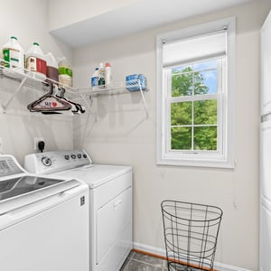 This functional laundry room features ample shelving, modern appliances, and natural light from a large window.