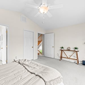 Spacious bedroom featuring light-colored walls, a ceiling fan, and easy access to an en-suite bathroom.