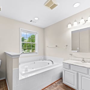 Spacious bathroom featuring a large jetted tub, dual sinks, and natural light from the nearby window.