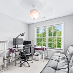 Bright and functional bedroom featuring a workspace, comfortable seating, and a large window with greenery views.