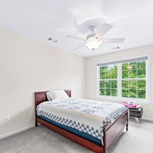 Bright bedroom featuring a large window, plush carpeting, and a ceiling fan for year-round comfort.
