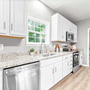Modern kitchen featuring stone countertops, stainless steel appliances, and abundant natural light from large windows.