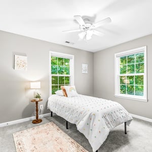 Bright and inviting bedroom featuring large windows, a ceiling fan, and comfortable furnishings for relaxation.