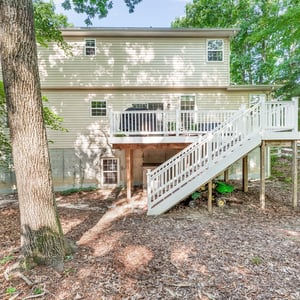 Spacious multi-level home nestled in a wooded area, featuring a large composite deck with stairs to the fenced-in backyard.