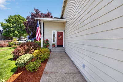 Inviting entryway features vibrant landscaping and a welcoming front porch with a bold red door.