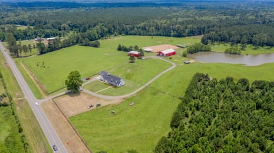 Spacious countryside property featuring a modern home, sprawling fields, a pond, and versatile outbuildings.