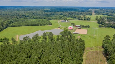 Sprawling countryside property with expansive fields, a tranquil pond, and multiple outbuildings for versatile use.