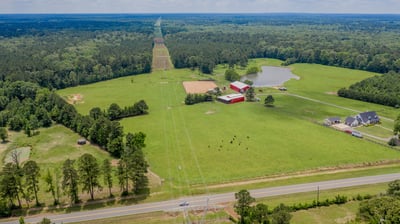 Expansive land with diverse terrain, ideal for agriculture or recreational use, featuring a picturesque pond and outbuildings.