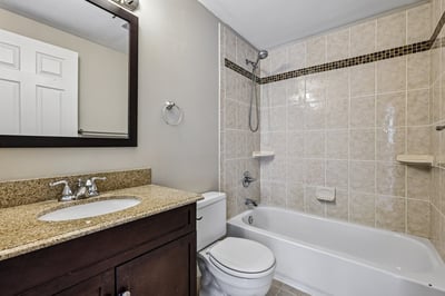 Modern bathroom featuring granite countertops, clean tilework, and a convenient shower-tub combination.