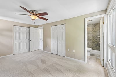 Spacious bedroom featuring a ceiling fan, multiple closets, and an adjoining bathroom for convenient living.