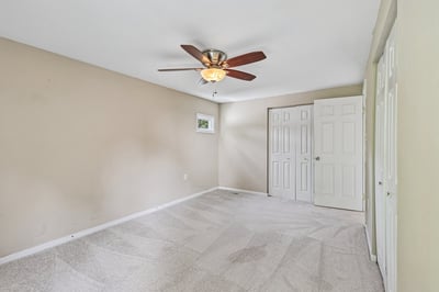 Spacious bedroom featuring a ceiling fan, large windows, and ample storage with double closets.