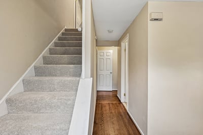 Bright and inviting entryway featuring carpeted stairs and warm hardwood floors, leading to a welcoming space.