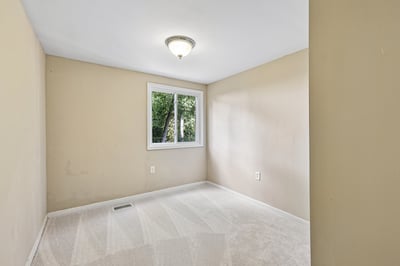Bright, empty room with fresh carpet and a large window offering natural light and outdoor views.
