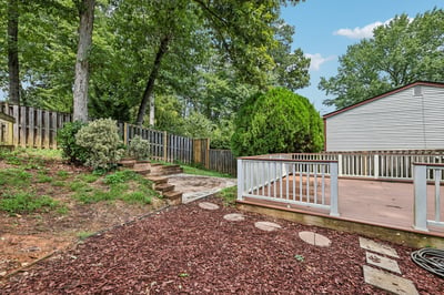 This inviting backyard features a spacious deck, lush greenery, and a stone pathway for easy access.