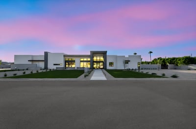 Exterior view at dusk with glowing interior lights and dramatic sky backdrop. This Paradise Valley home offers stunning evening curb appeal.