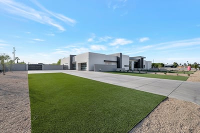 South-facing view featuring a long driveway, green lawn, and contemporary exterior. This Paradise Valley property offers a spacious lot with modern curb appeal and clean landscaping.