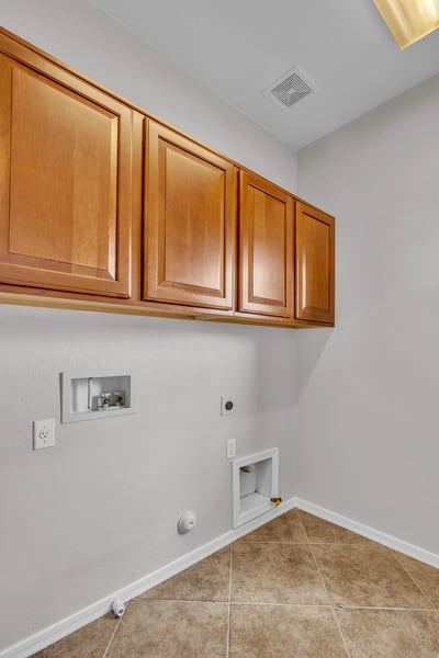 Functional laundry room with overhead cabinets and durable tile flooring, adding convenience and storage space.