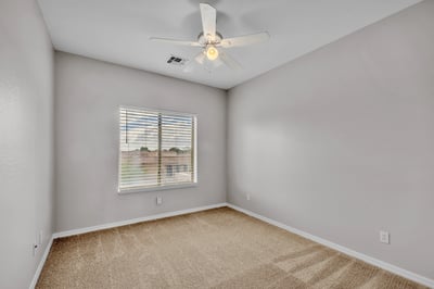 Comfortable bedroom with plush carpet, ceiling fan, and natural light, ideal for guests or a home office setup in Goodyear.