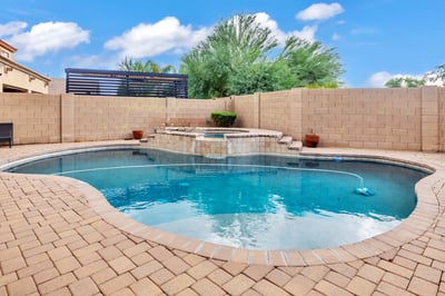 Stylish pool with raised spa and water feature, complemented by paver decking and privacy walls for a serene backyard setting in Goodyear.