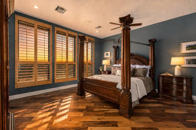 Warm and inviting primary suite highlighted by glowing sunset views, plantation shutters, and beautiful hardwood floors. A peaceful retreat designed for comfort and relaxation.